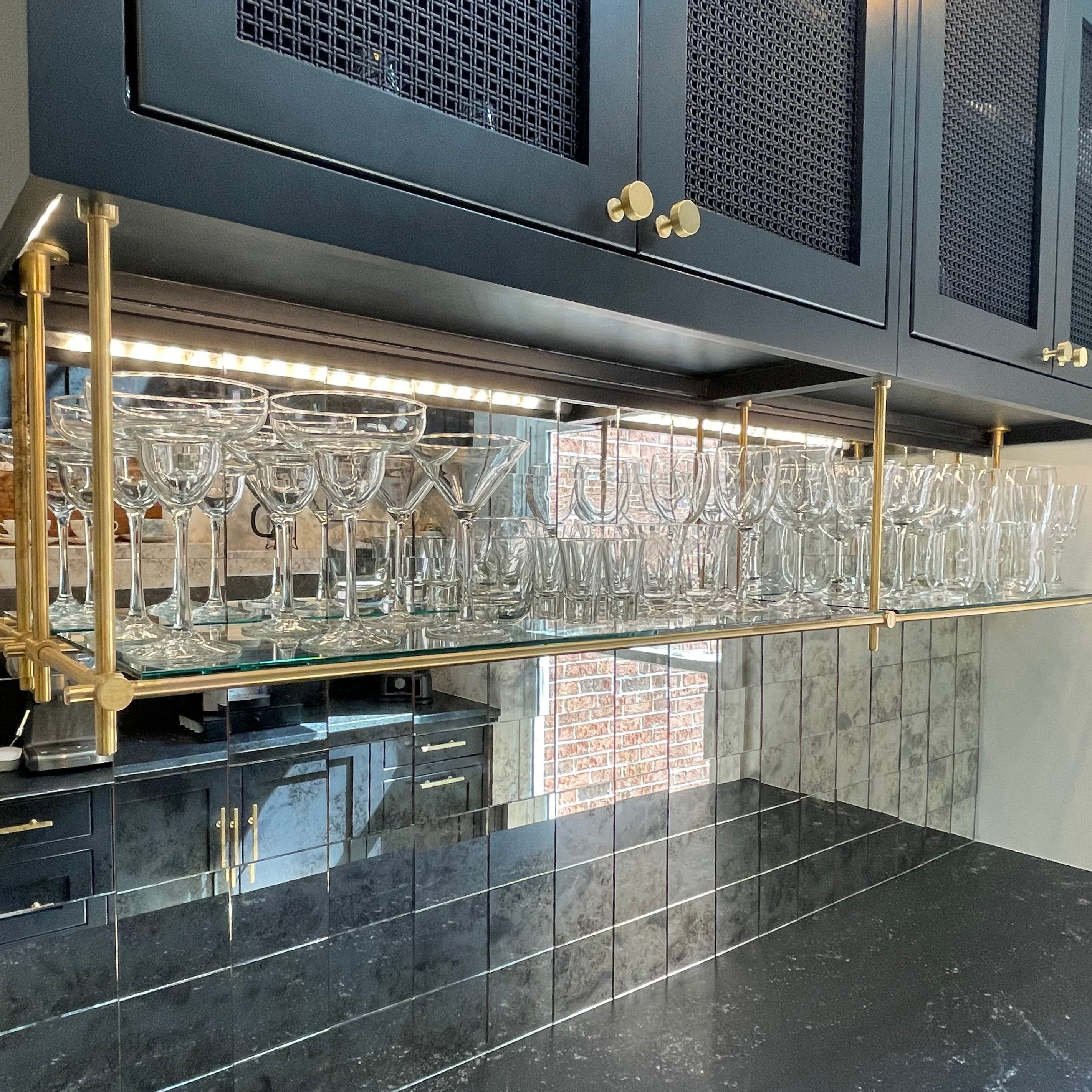 Elegant brass shelving unit with glass holders, perfect for modern kitchens and bars. Featuring a sleek black and gold design, this brass shelving system provides stylish and functional storage for glassware. Ideal for showcasing wine glasses and other drinkware in a sophisticated setting.