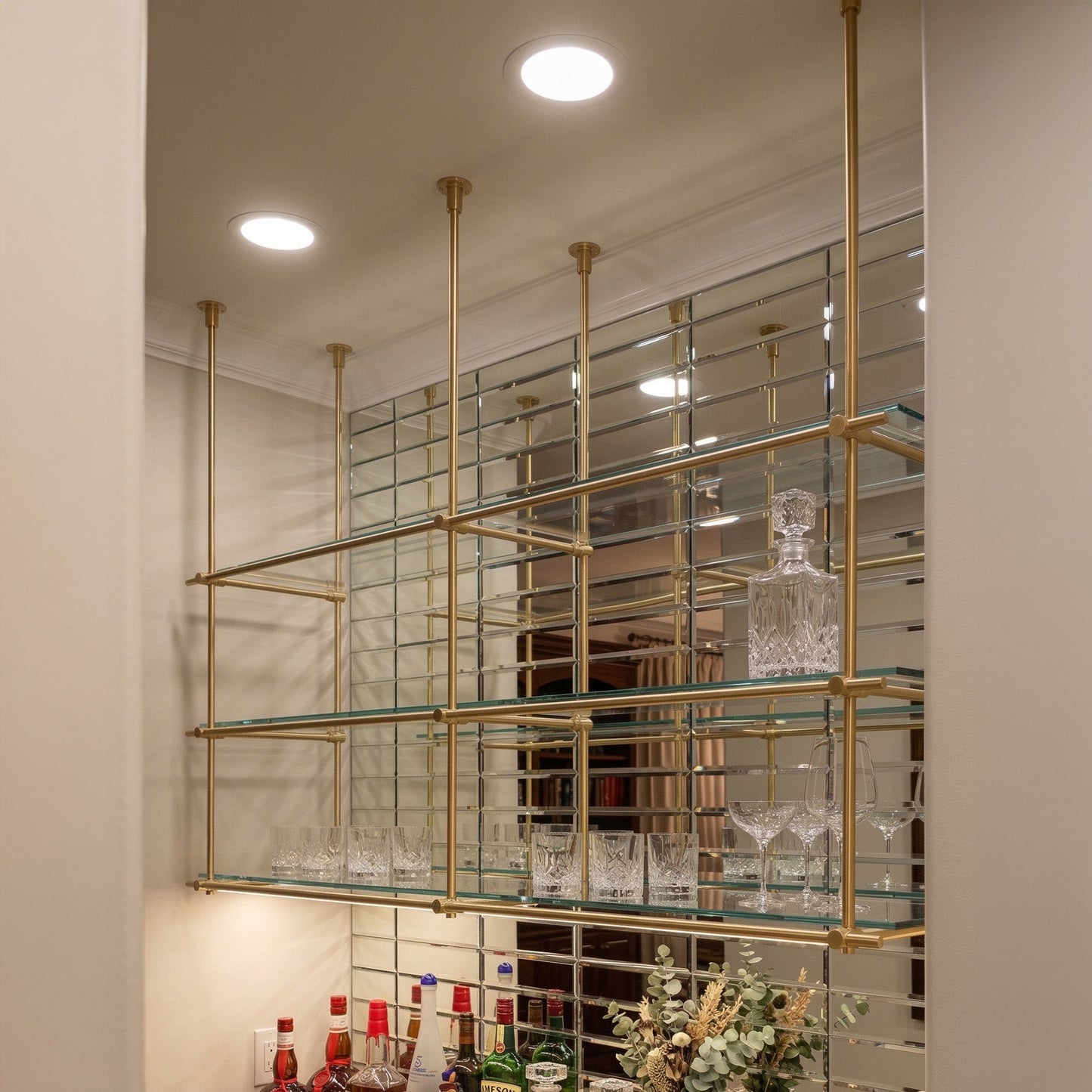 Ceiling-mounted solid brass shelving with glass shelves in a luxury home bar, unlacquered brass finish, BrassShelf