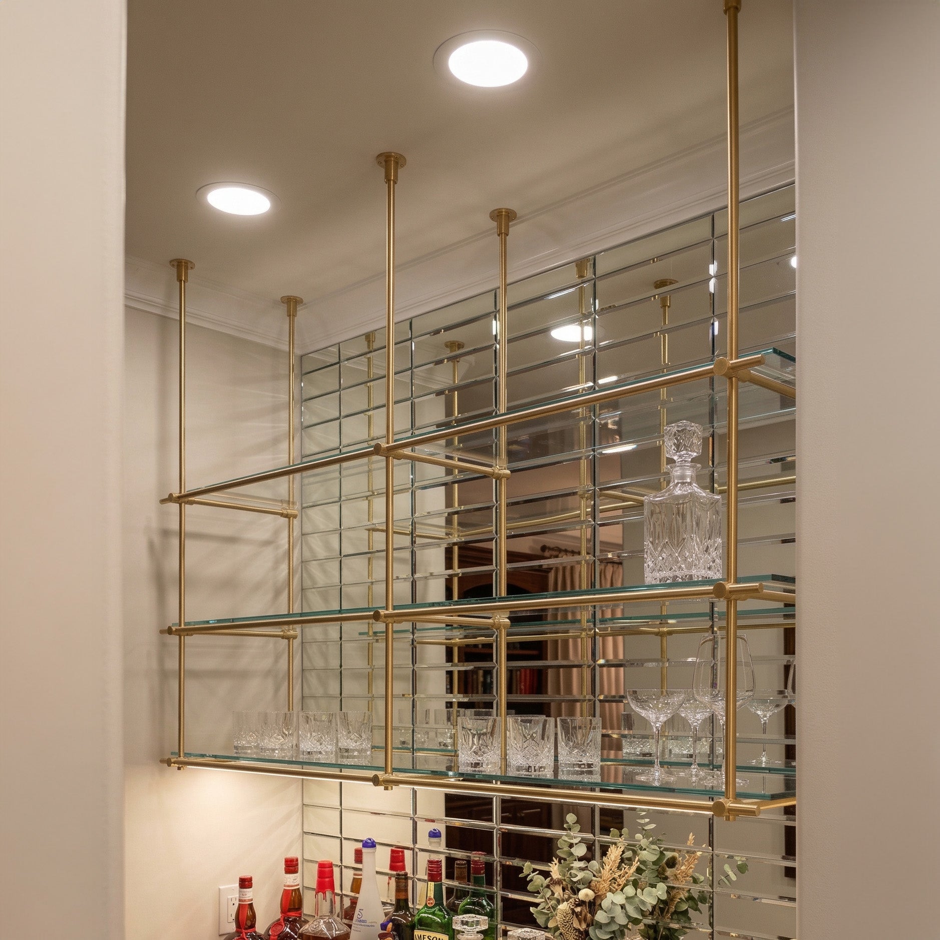 Ceiling-mounted solid brass shelving with glass shelves in a luxury home bar, unlacquered brass finish, BrassShelf
